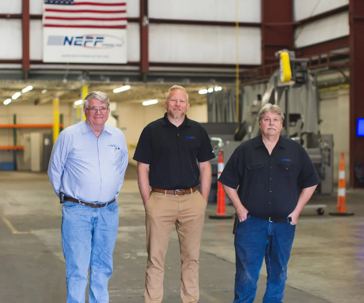 P1 Three men standing in a warehouse with their hands on their hips.